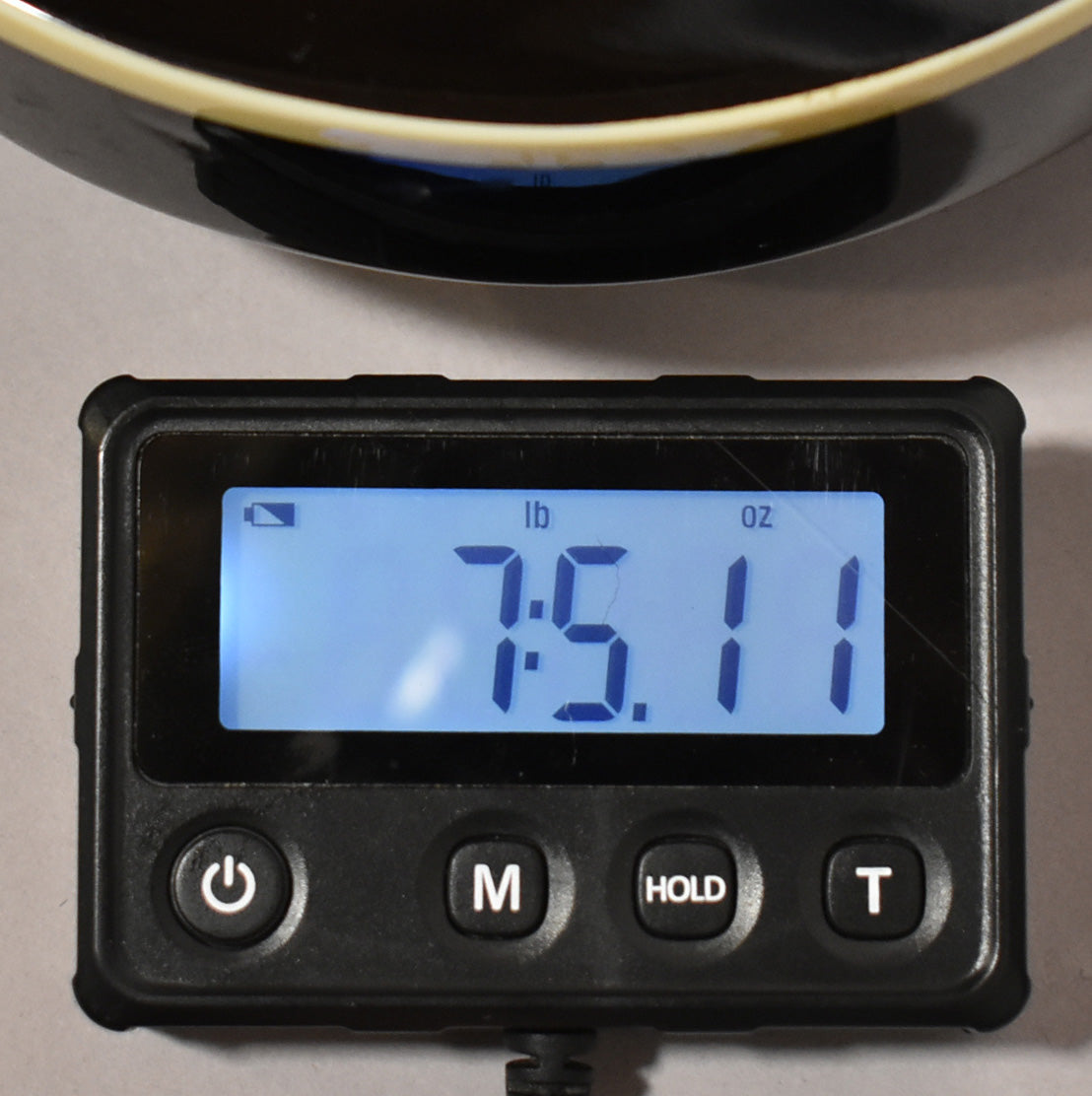A digital scale displays the guitar's weight as 7 pounds, 5.11 ounces, with a dark, curved object partially visible above.
