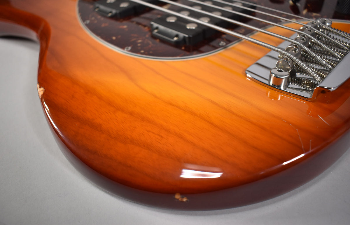 Close-up of the bass body's lower bout, showing the honey sunburst finish, two humbuckers, chrome bridge, and several dings and scratches.