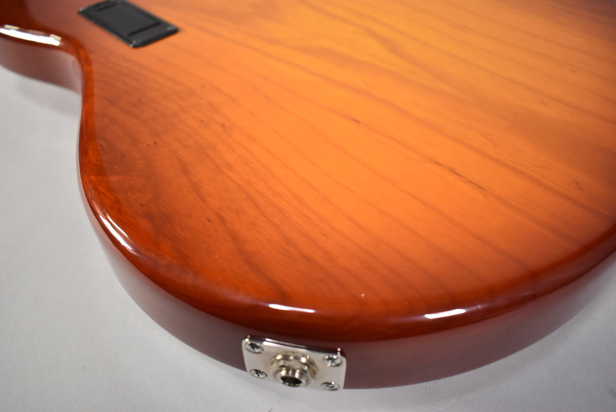 Close-up of the bass body's lower bout, showing the glossy honey sunburst finish, output jack, and a few minor surface scratches.