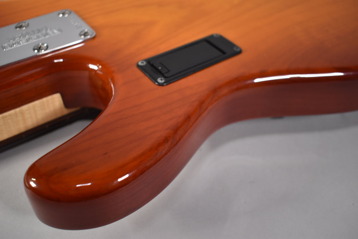 Close-up of the bass's lower body, showing the honey sunburst finish, neck plate, and a black rectangular battery compartment.