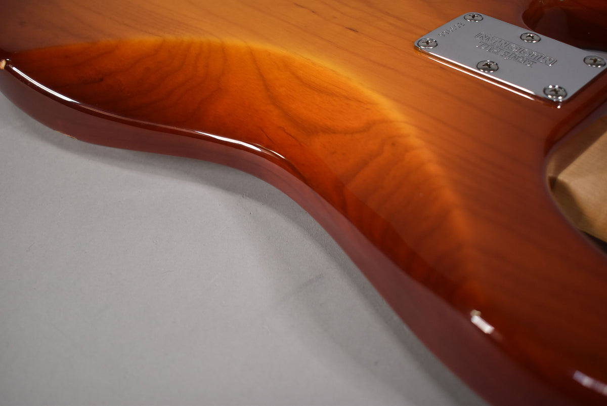 Close-up of the bass's upper body, showing the honey sunburst finish, wood grain, and a small chip on the top edge.