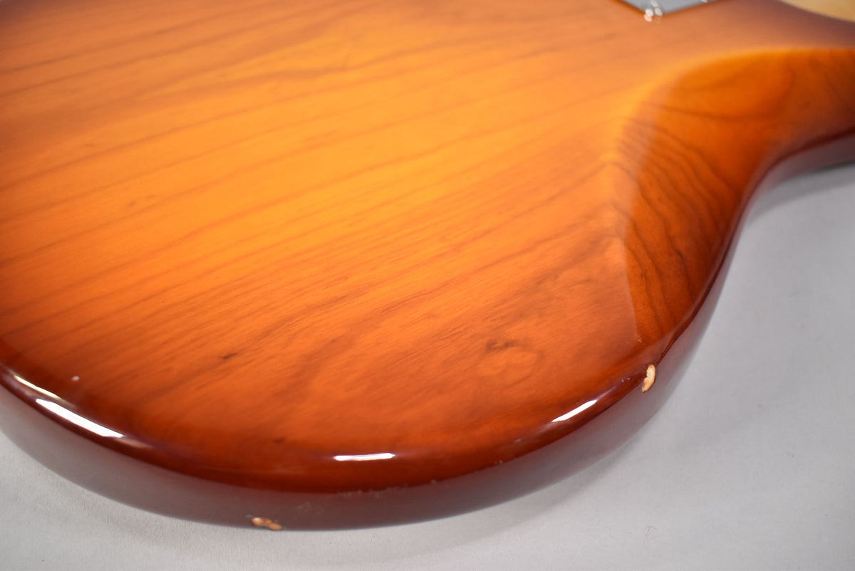 Close-up of the bass body's lower bout, showing the honey sunburst finish, wood grain, and several small chips along the bottom edge.