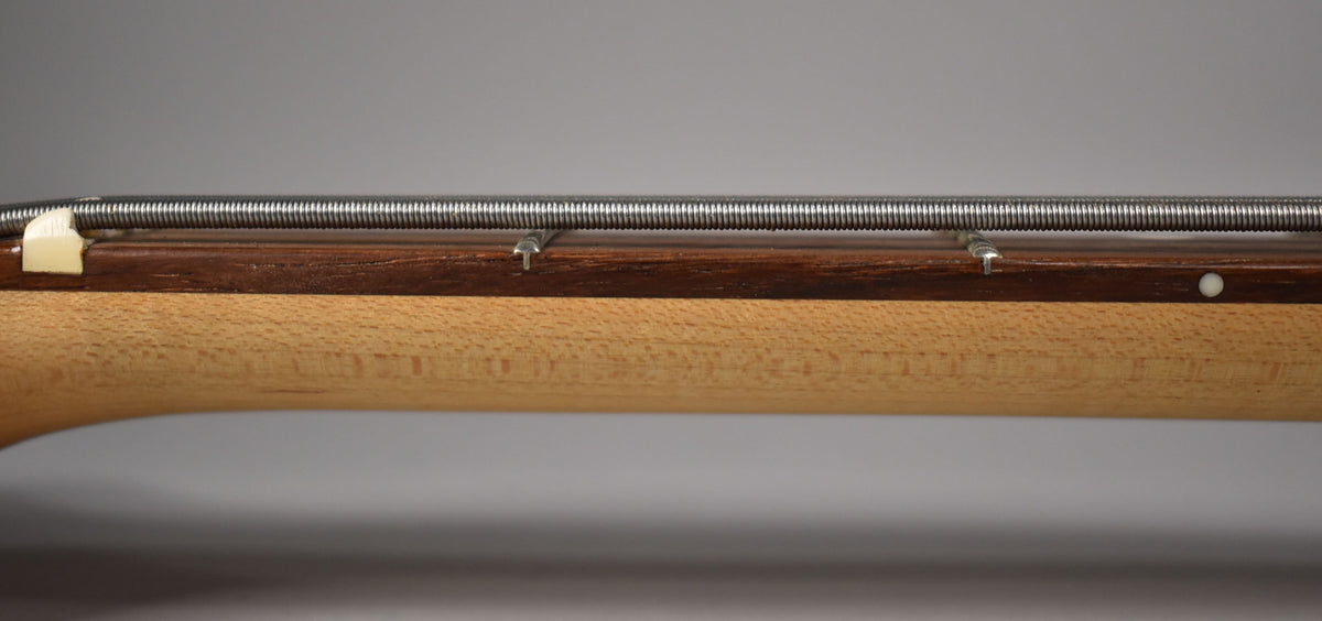 Close-up of the bass neck from the side, showing the light maple neck, dark rosewood fretboard, nut, and five strings.