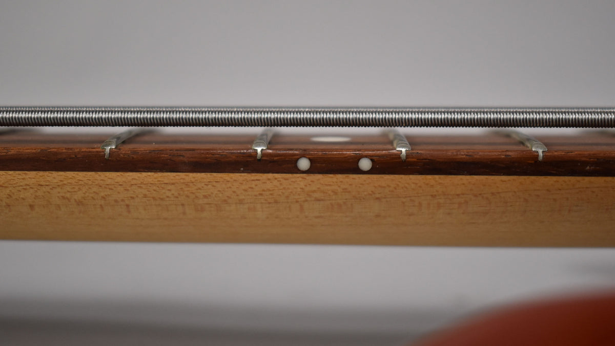 Close-up of the bass neck and fretboard, showing the side dots and a single string running above the frets.