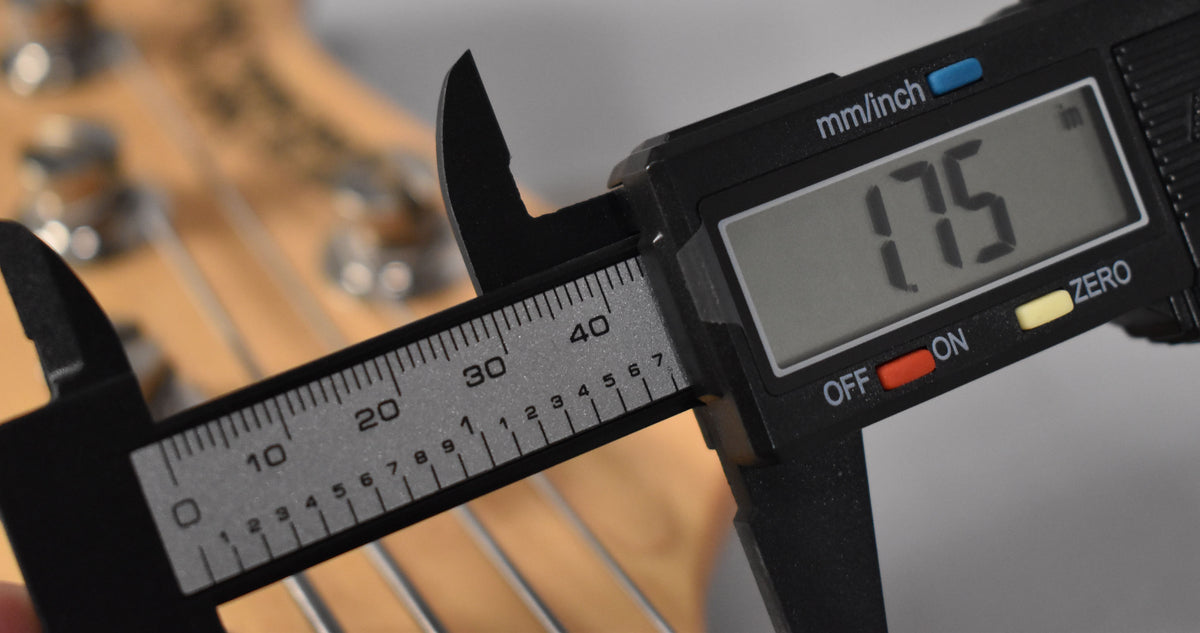 A digital caliper measures the bass's nut width at 1.75 inches, with the headstock and strings visible in the background.