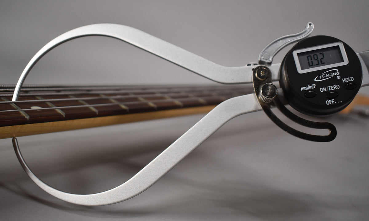 A digital caliper measures the bass's string action at 0.92, showing the fretboard, frets, and strings.