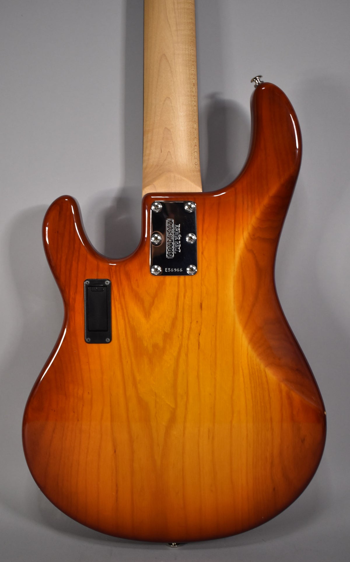 Rear view of a honey sunburst bass guitar, showing the neck joint, chrome neck plate, and a black rectangular battery compartment.