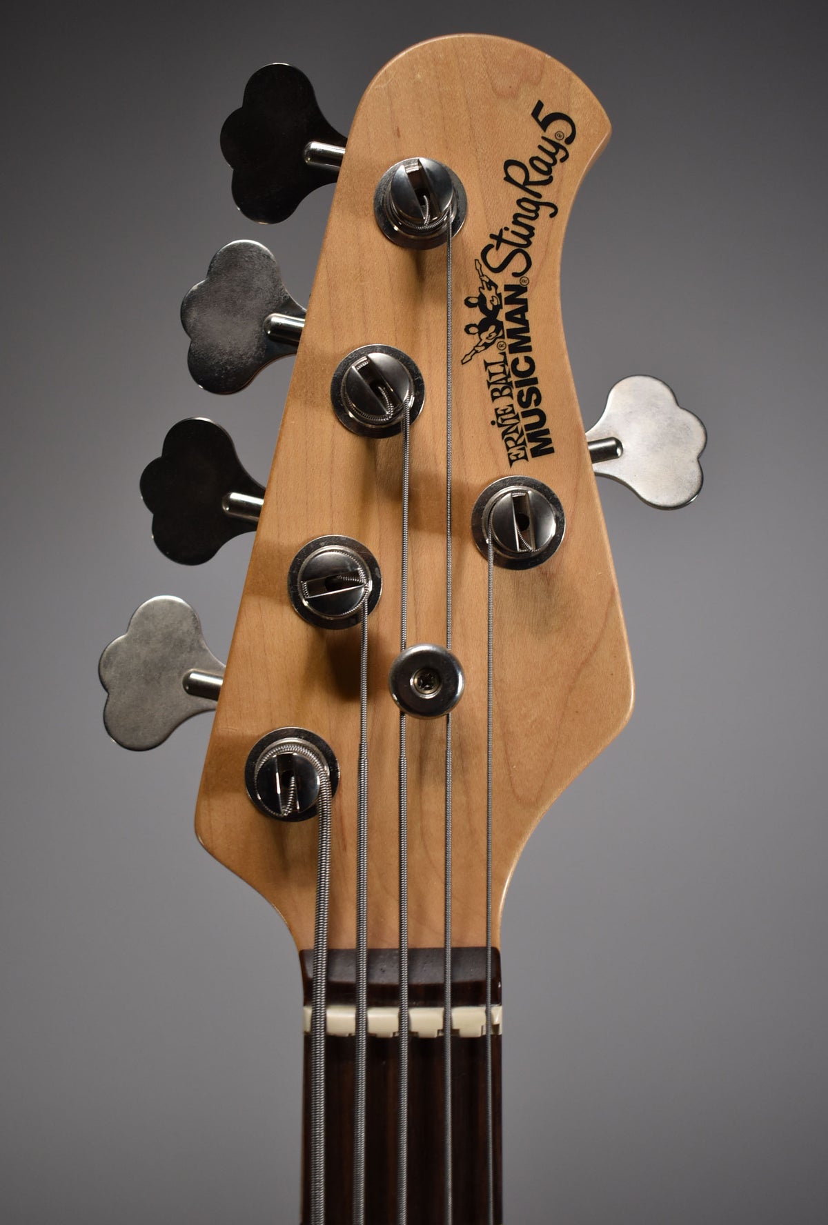 Close-up of the bass headstock, showing five clover-leaf tuners, a string tree, and the nut with five strings.