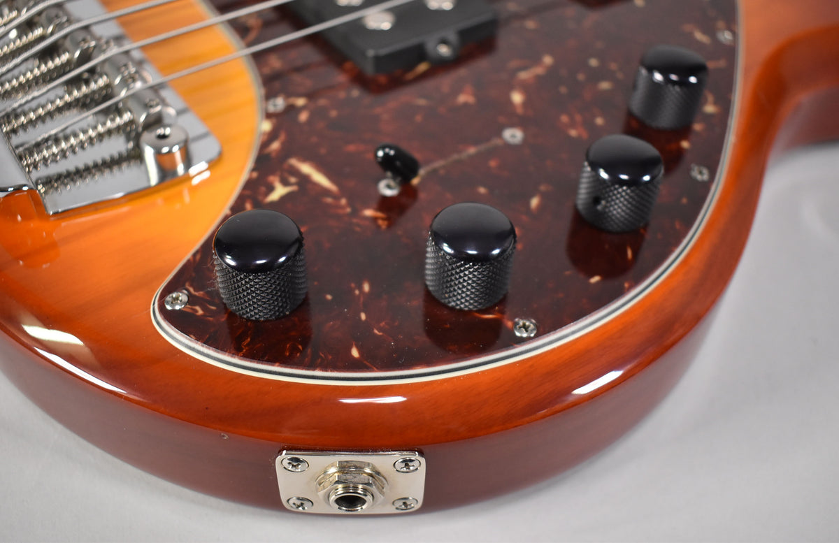 Close-up of the bass's lower body, showing the honey sunburst finish, tortoiseshell pickguard, four black knurled control knobs, and output jack.