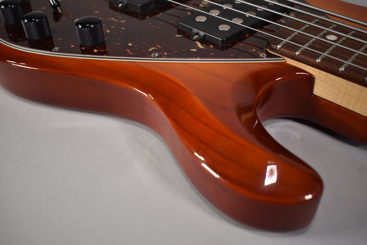 Upper body of a honey sunburst bass, showing the glossy finish, tortoise pickguard, black knobs, and two humbucker pickups.