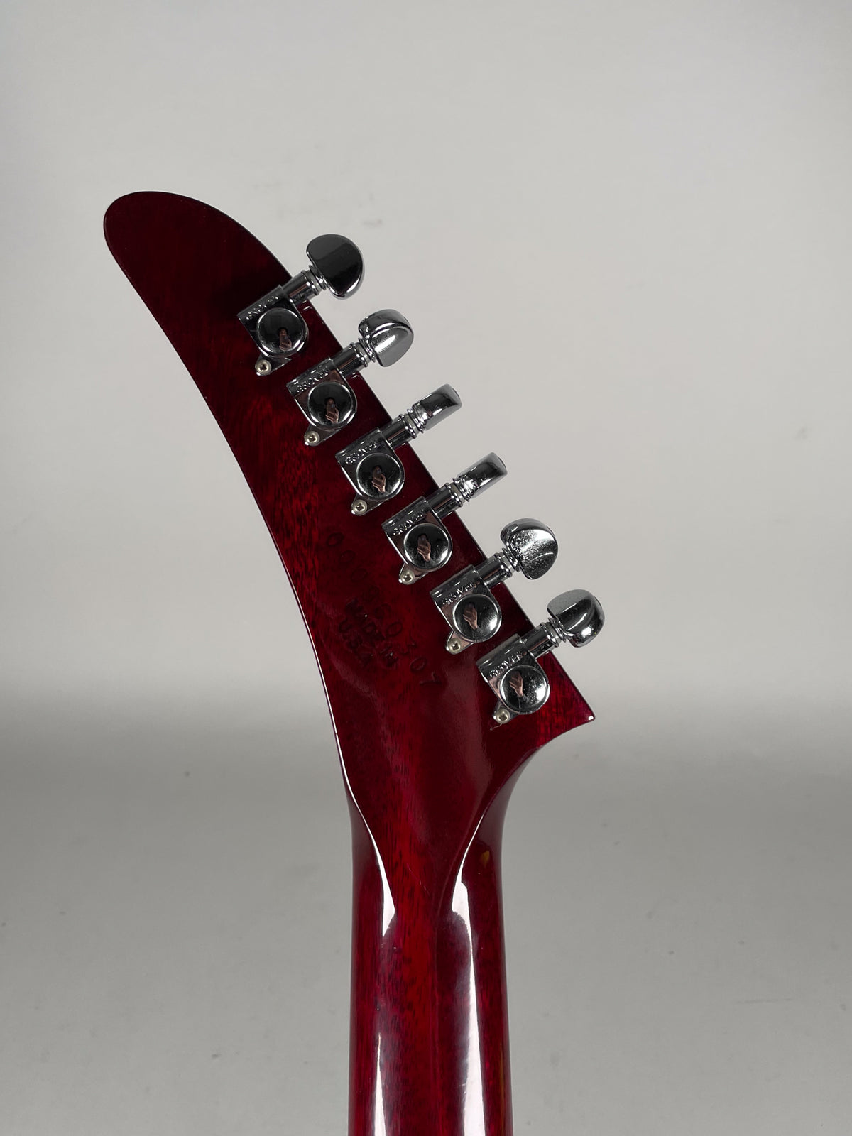 The back of a wine red guitar headstock and neck, showing six chrome tuners with small circular buttons.