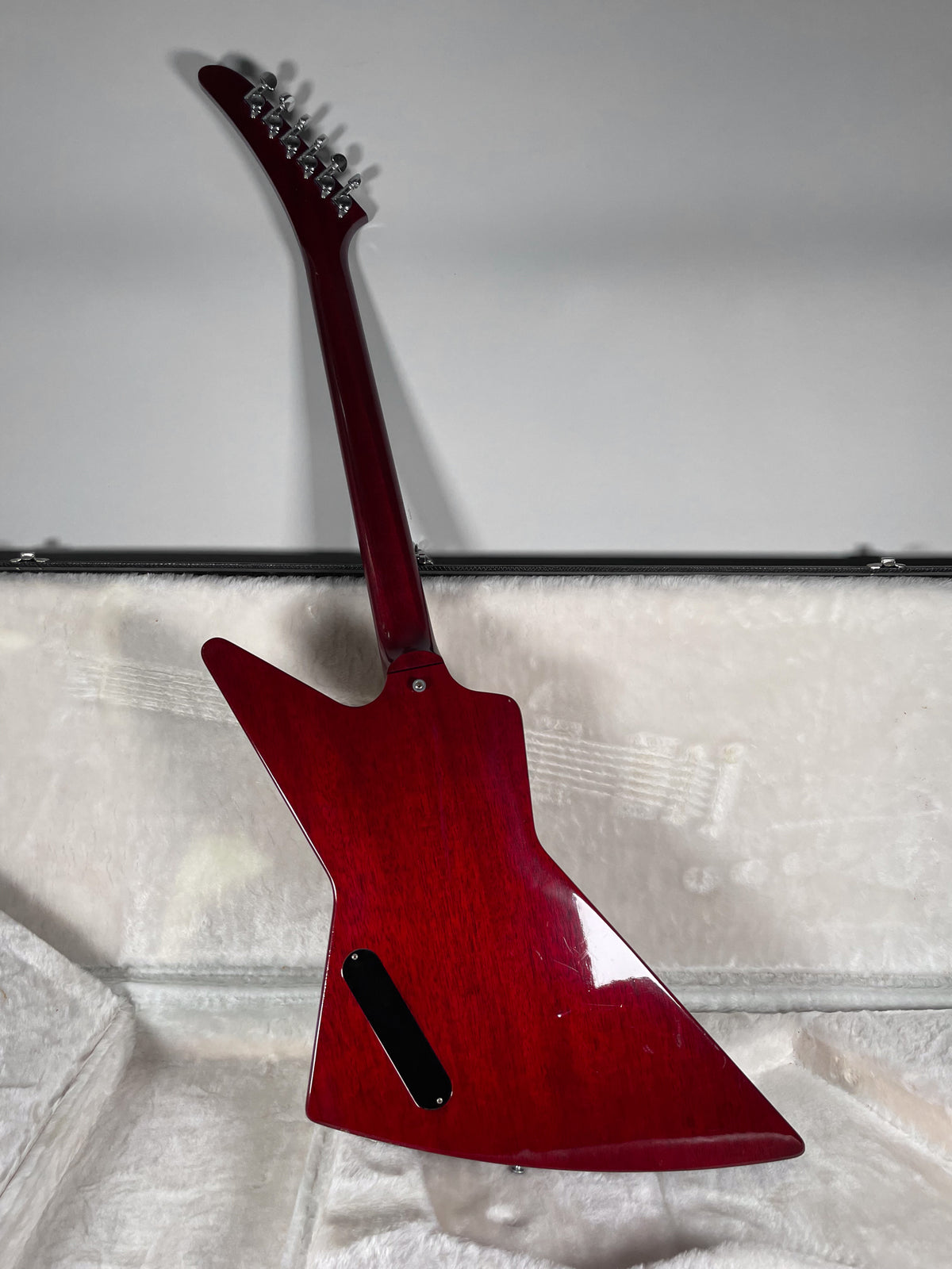 The back of a wine red electric guitar with a glossy finish, showing some light scratches, rests in a white plush-lined case.