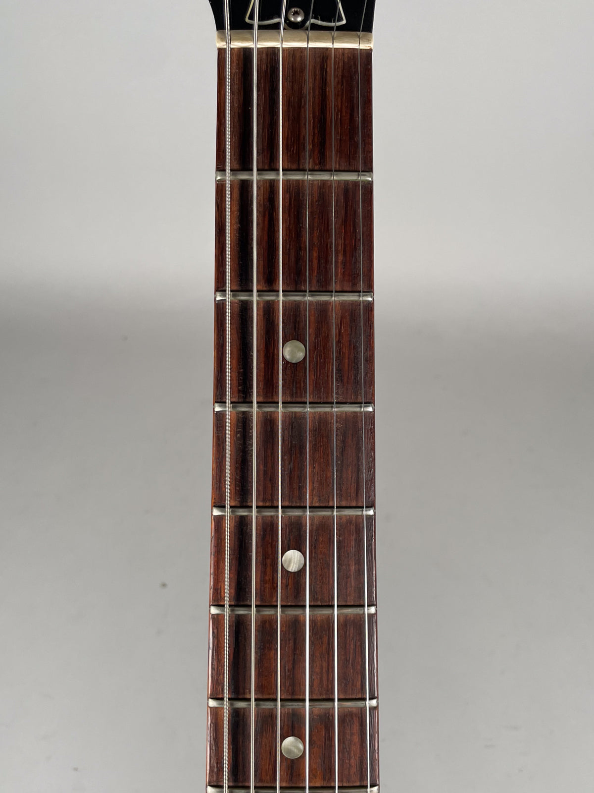 Close-up of the dark rosewood fretboard with pearloid dot inlays, showing frets 1 through 10 and the guitar's strings.