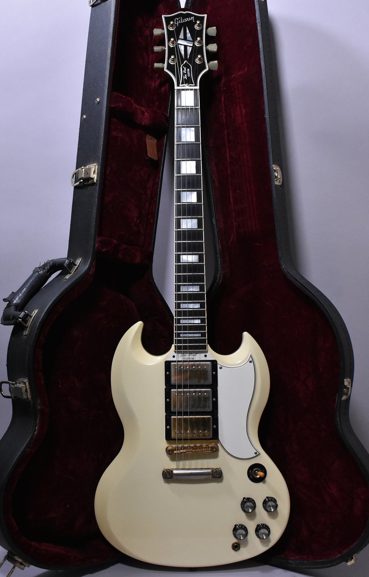 Full-length view of an Alpine White SG-style guitar with three humbuckers, gold hardware, and a white pickguard, resting in its open case.