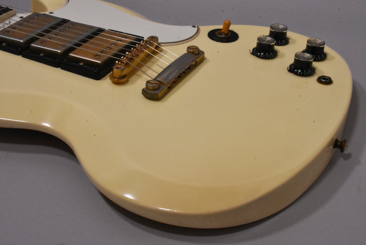 Close-up of the cream-colored body, showing two gold humbuckers, a tune-o-matic bridge, four black control knobs, and a toggle switch.