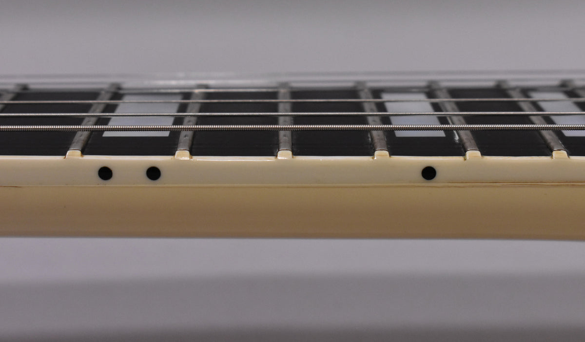 Close-up of the guitar's cream-bound ebony fretboard with block inlays and side dots, showing light wear on the frets.