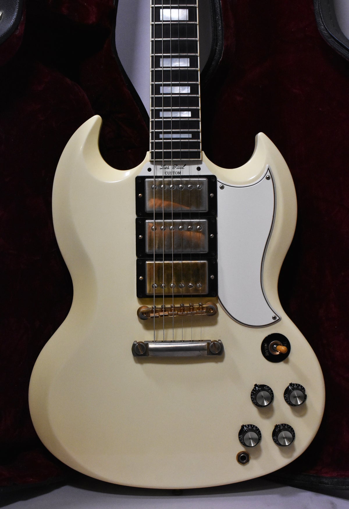 Full view of the cream-colored SG body with three humbuckers, a white pickguard, and four black control knobs.