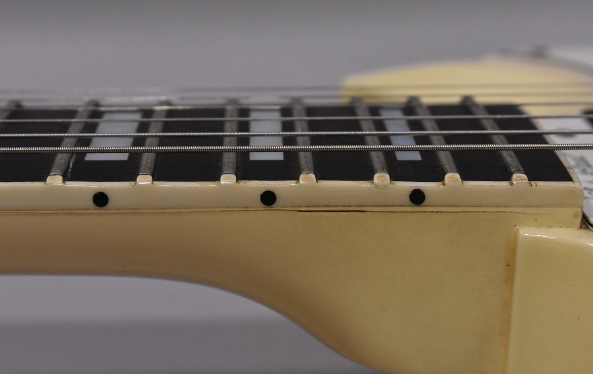 Close-up of the Alpine White neck binding and dark fretboard with block inlays, showing light finish checking along the binding.