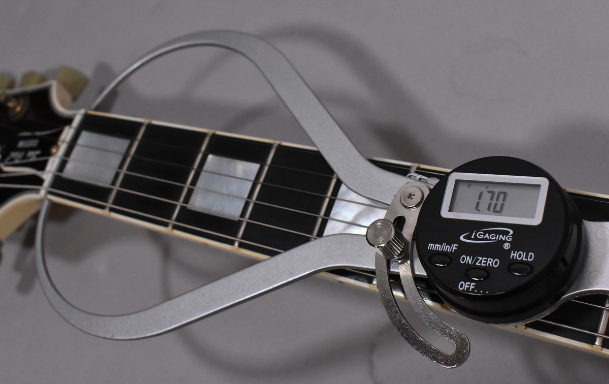 A digital caliper measures the guitar's fretboard, showing "1.70" on its display, with block inlays visible on the dark fretboard.