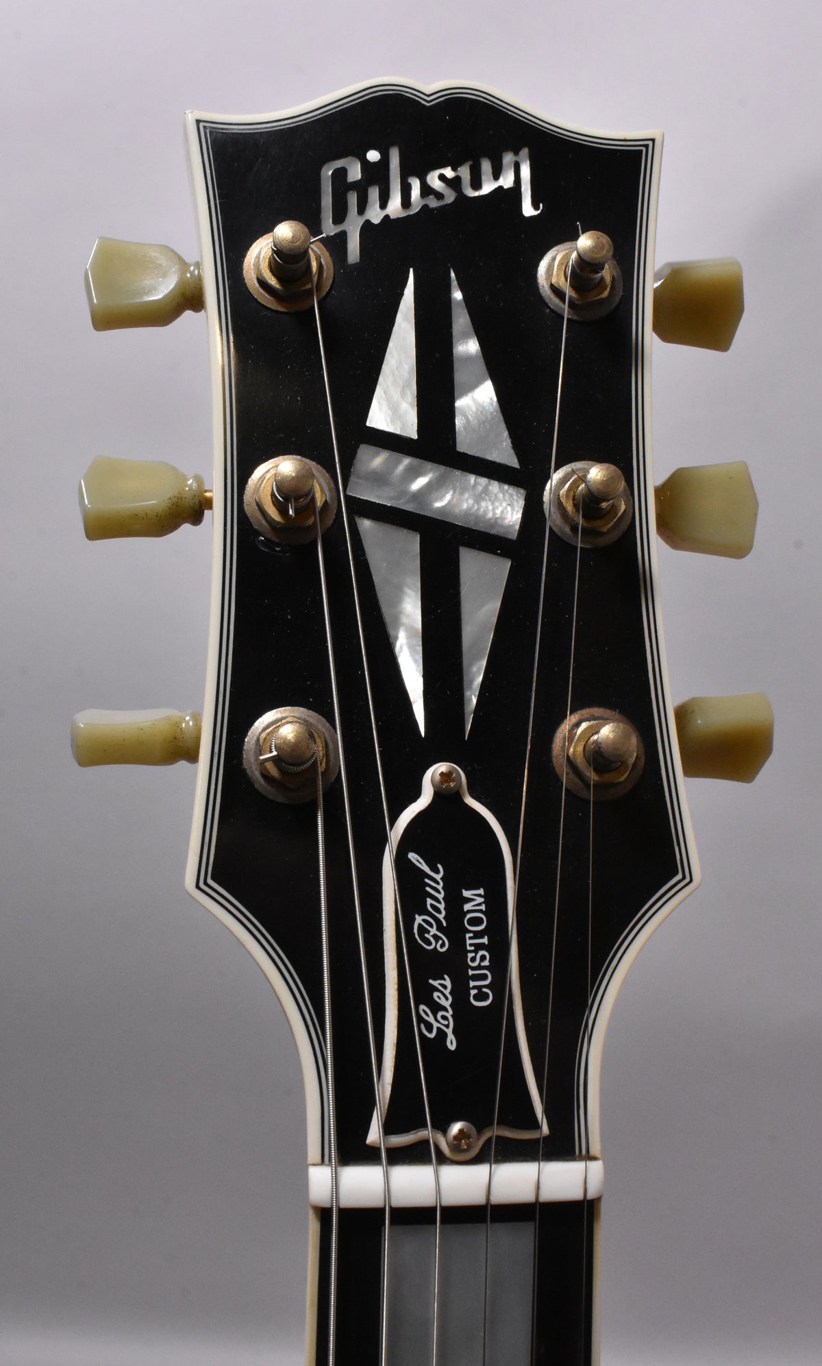 Close-up of the black headstock with white binding, showing six aged gold tuners with green-yellow buttons and mother-of-pearl inlays.