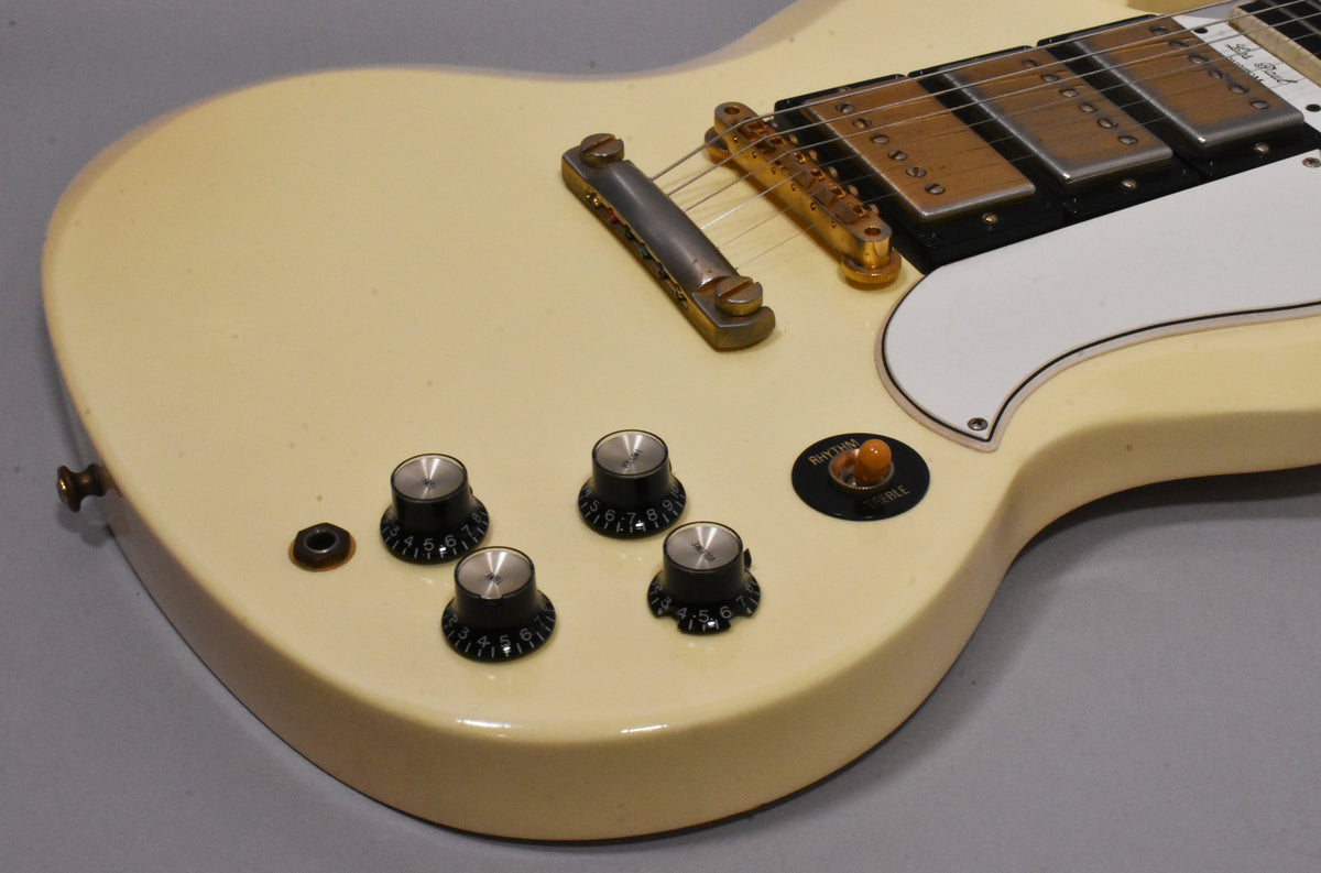 Close-up of the guitar's lower body, showing the aged Alpine White finish, four black control knobs, and a three-way toggle switch.