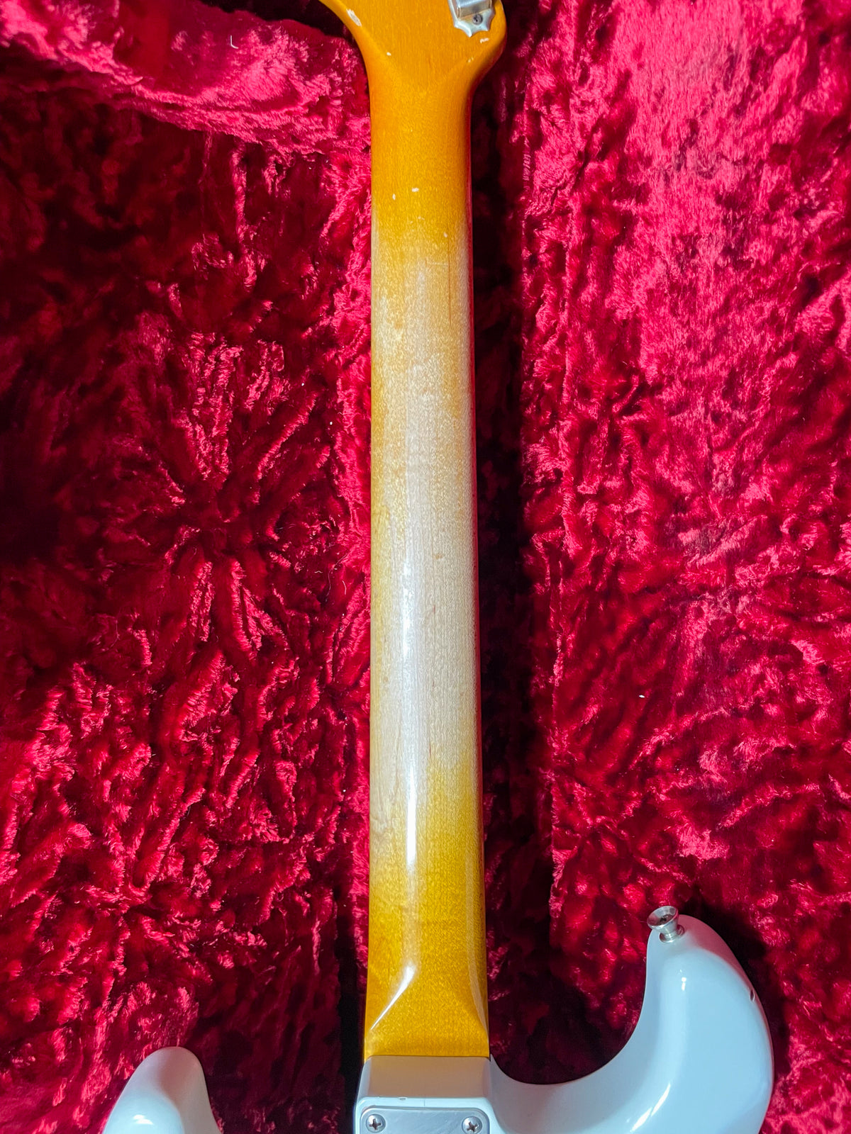The guitar's maple neck, with a worn relic finish, is viewed from behind, showing the heel and part of the Olympic White body.