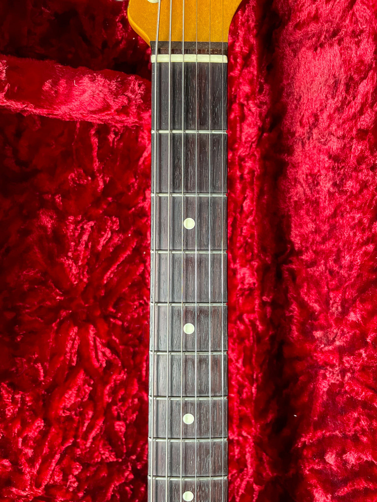 Close-up of the guitar's dark fretboard with white dot inlays, showing frets 1-10, against a plush red case lining.