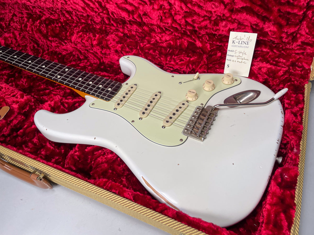 Olympic white guitar, angled in a red velvet case, shows heavy relic wear on the lower bout and a mint green pickguard.