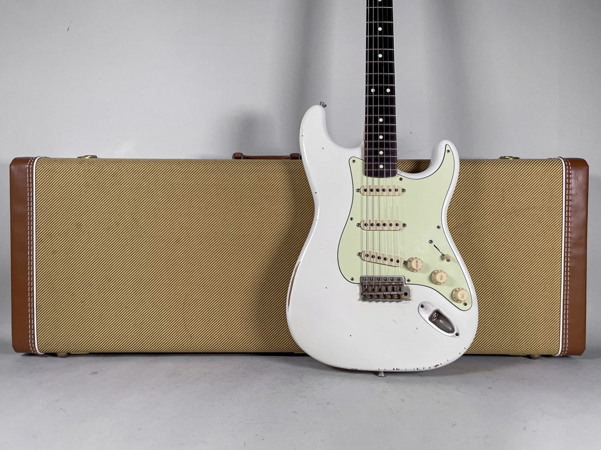 Full view of an Olympic White relic guitar with a mint green pickguard, standing upright in front of a tweed hard shell case.