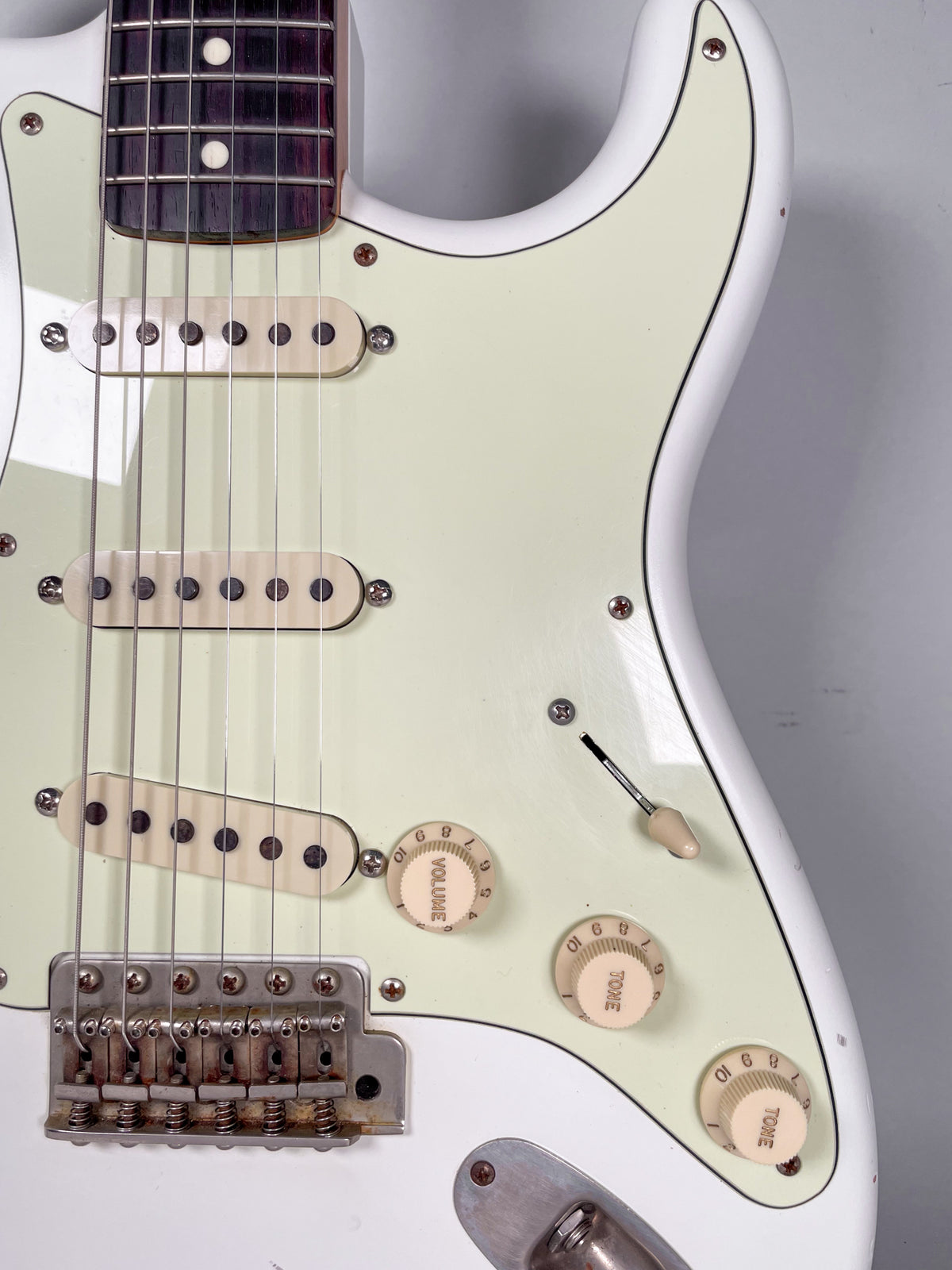The Olympic White relic body, with a mint green pickguard, shows three cream single-coil pickups and aged chrome hardware.