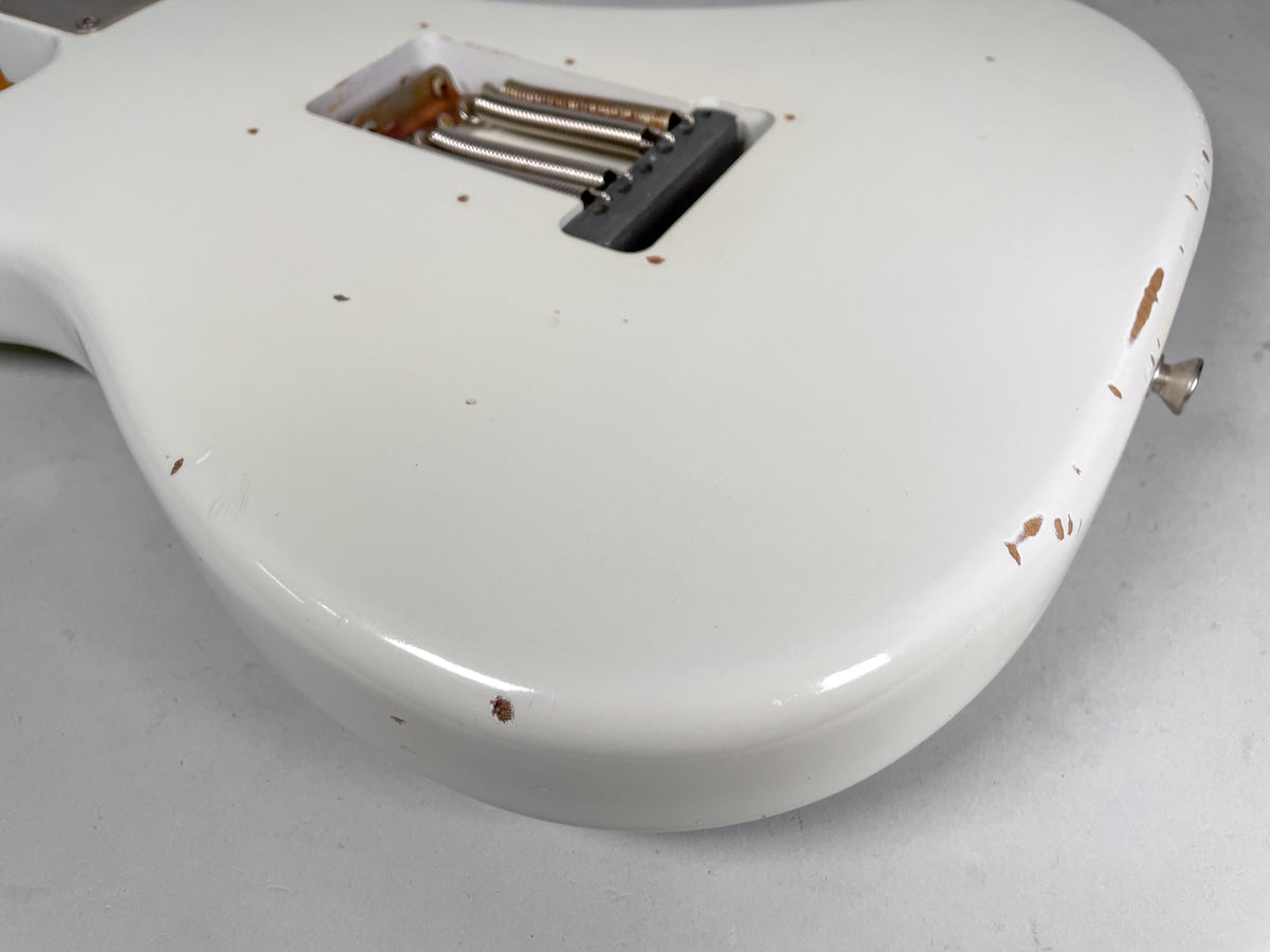 The back of the Olympic White guitar body, showing the tremolo spring cavity and heavy relic wear with exposed wood on the edges.