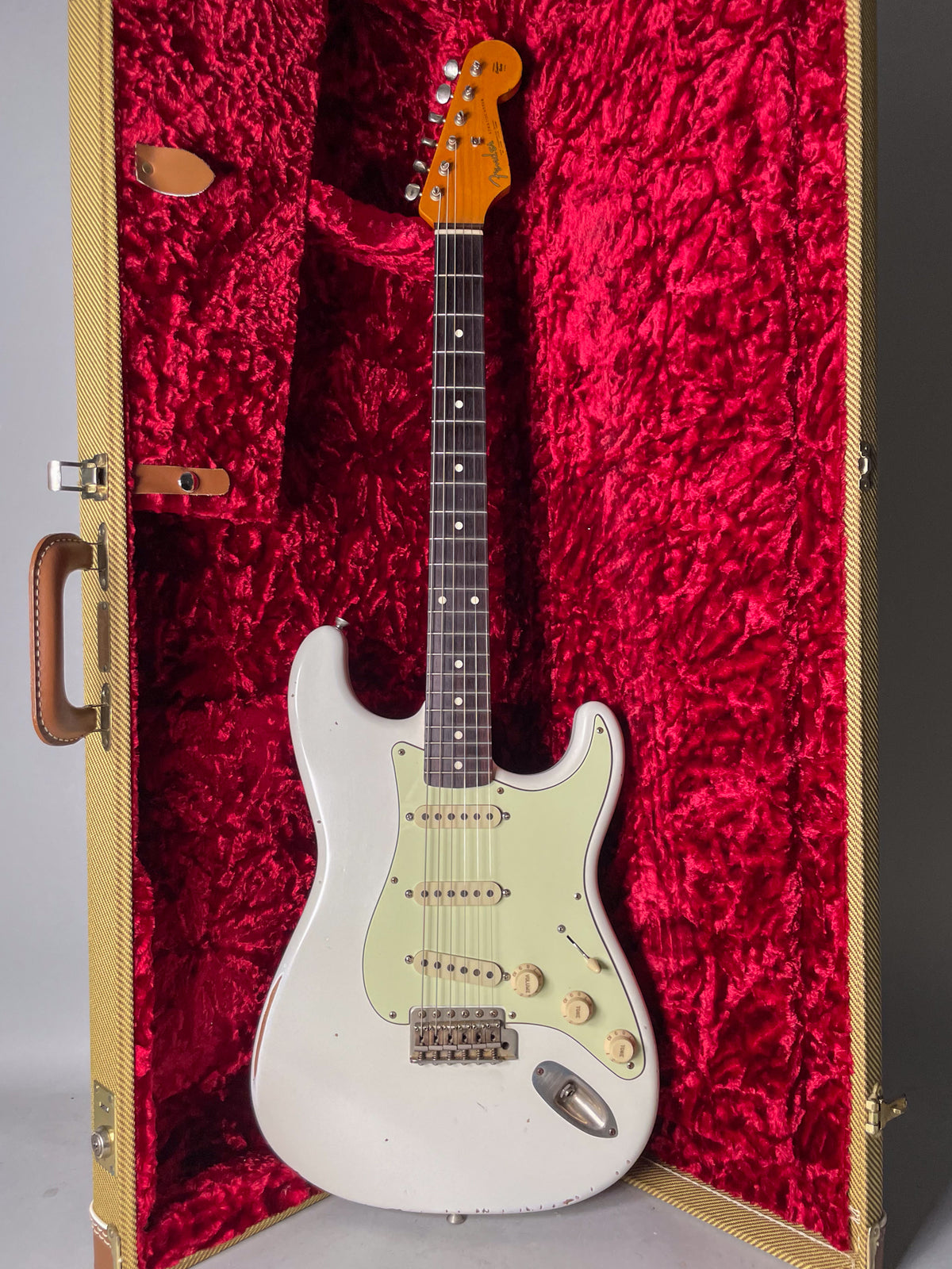 Full view of an Olympic White relic S-type guitar with a mint green pickguard, in a tweed hard case with red crushed velvet lining.