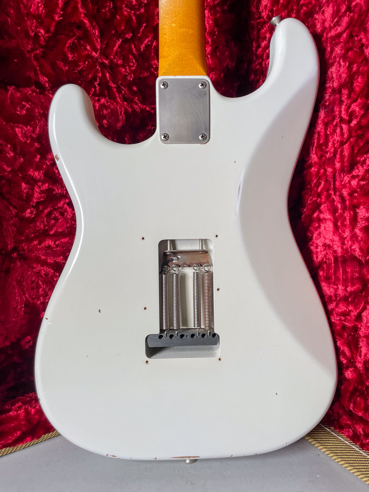 Back of an Olympic White guitar, showing the tremolo cavity with three springs, a neck plate, and relic wear.