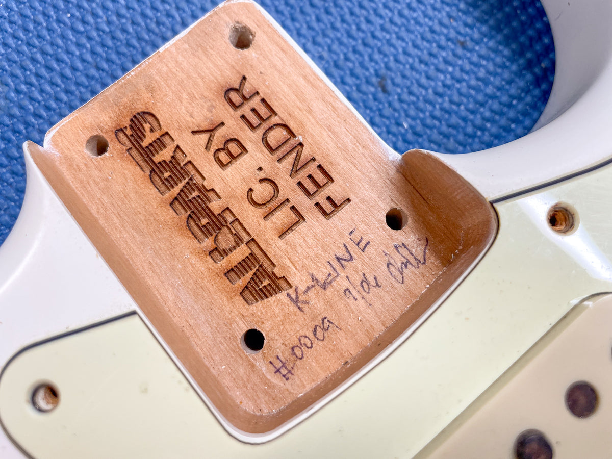 Close-up of the guitar's neck pocket, showing exposed wood with stamped and handwritten markings, and the Olympic White body.