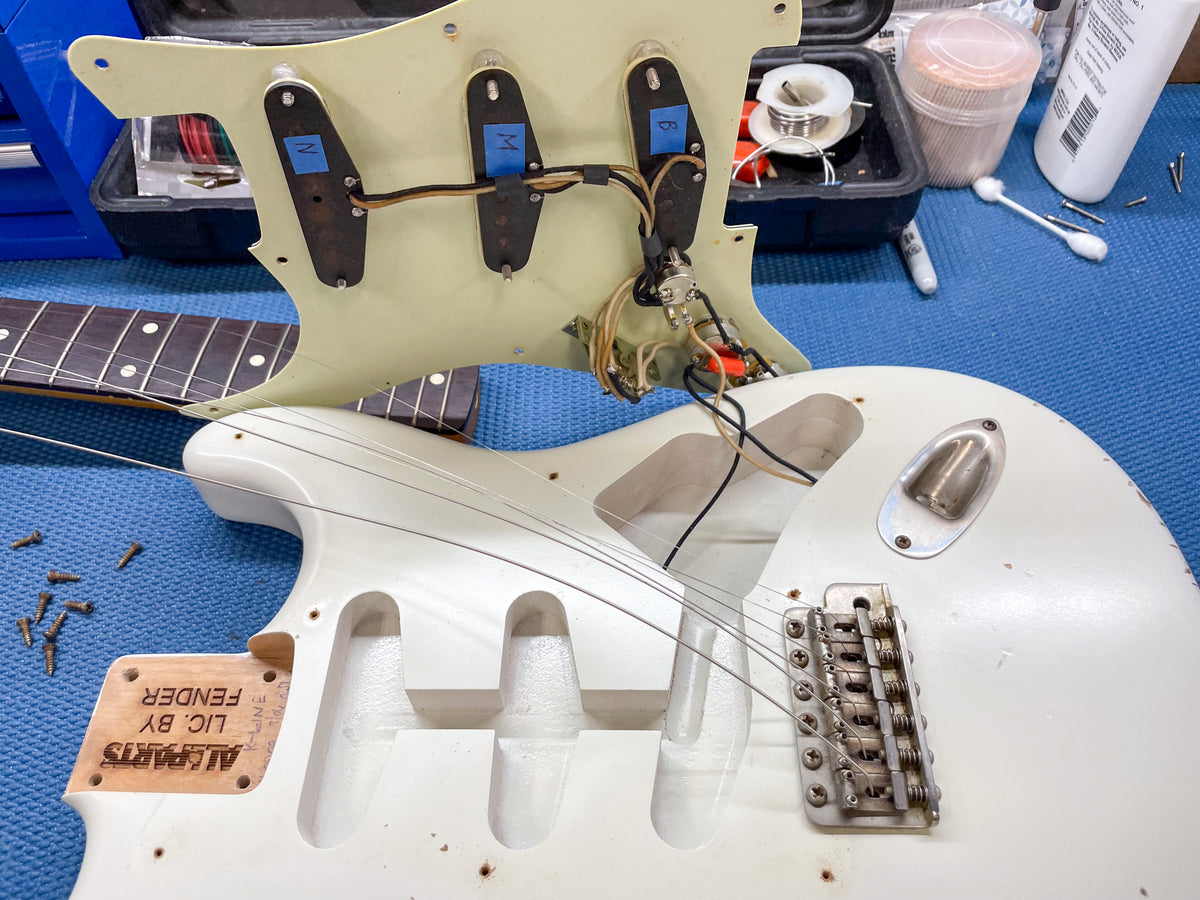 The Olympic White body is shown with the pickguard lifted, revealing the pickups, wiring, tremolo bridge, and output jack.