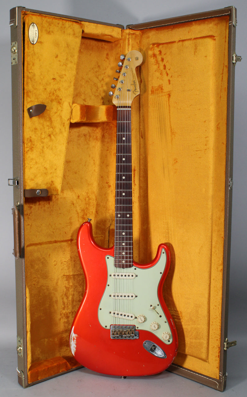 Full-length view of a bright orange Stratocaster with a mint green pickguard, white pickups, and heavy relic wear, standing in its open, gold-lined case.