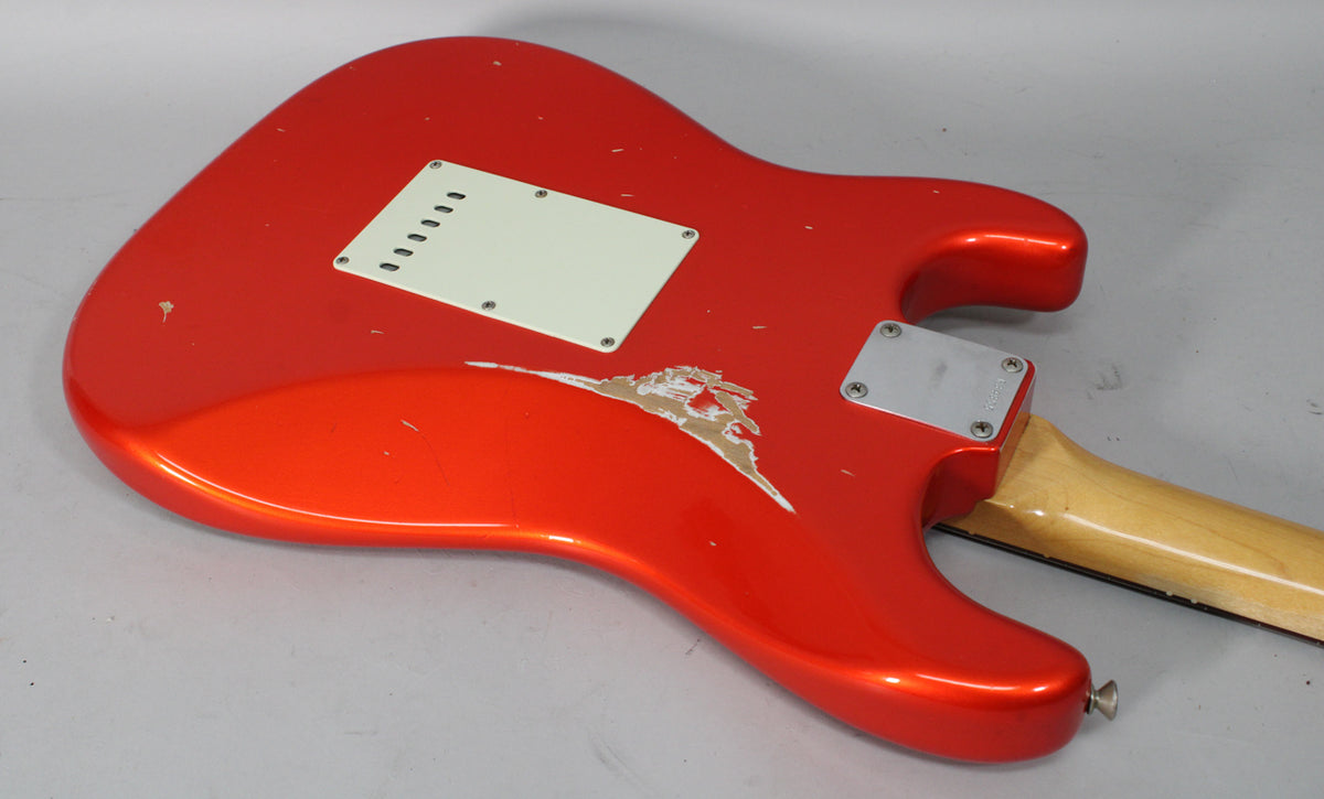 The back of a Candy Tangerine Stratocaster, showing a large area of chipped paint exposing the wood, and a white tremolo cover.