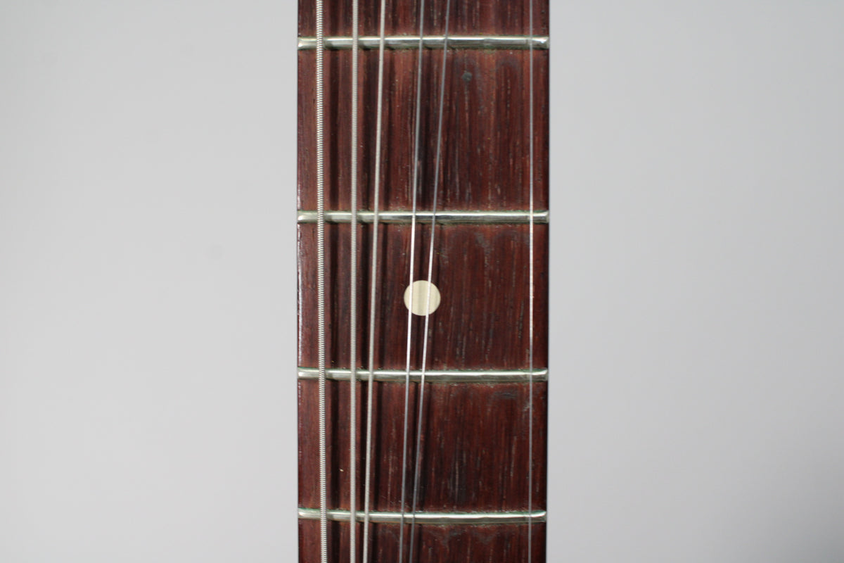 Close-up of the dark rosewood fretboard with six strings, frets, and a single cream-colored dot inlay at the 7th fret.