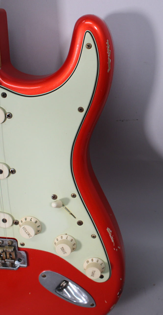 Close-up of the guitar's lower body, showing the candy tangerine finish with heavy relic wear, mint green pickguard, and three cream control knobs.
