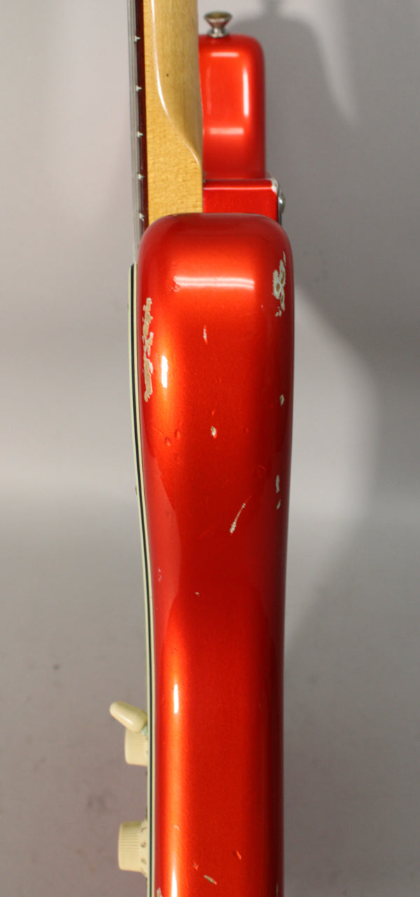 The guitar's candy tangerine body, seen from the side, shows heavy relic wear with large chips and scratches revealing the lighter wood underneath.