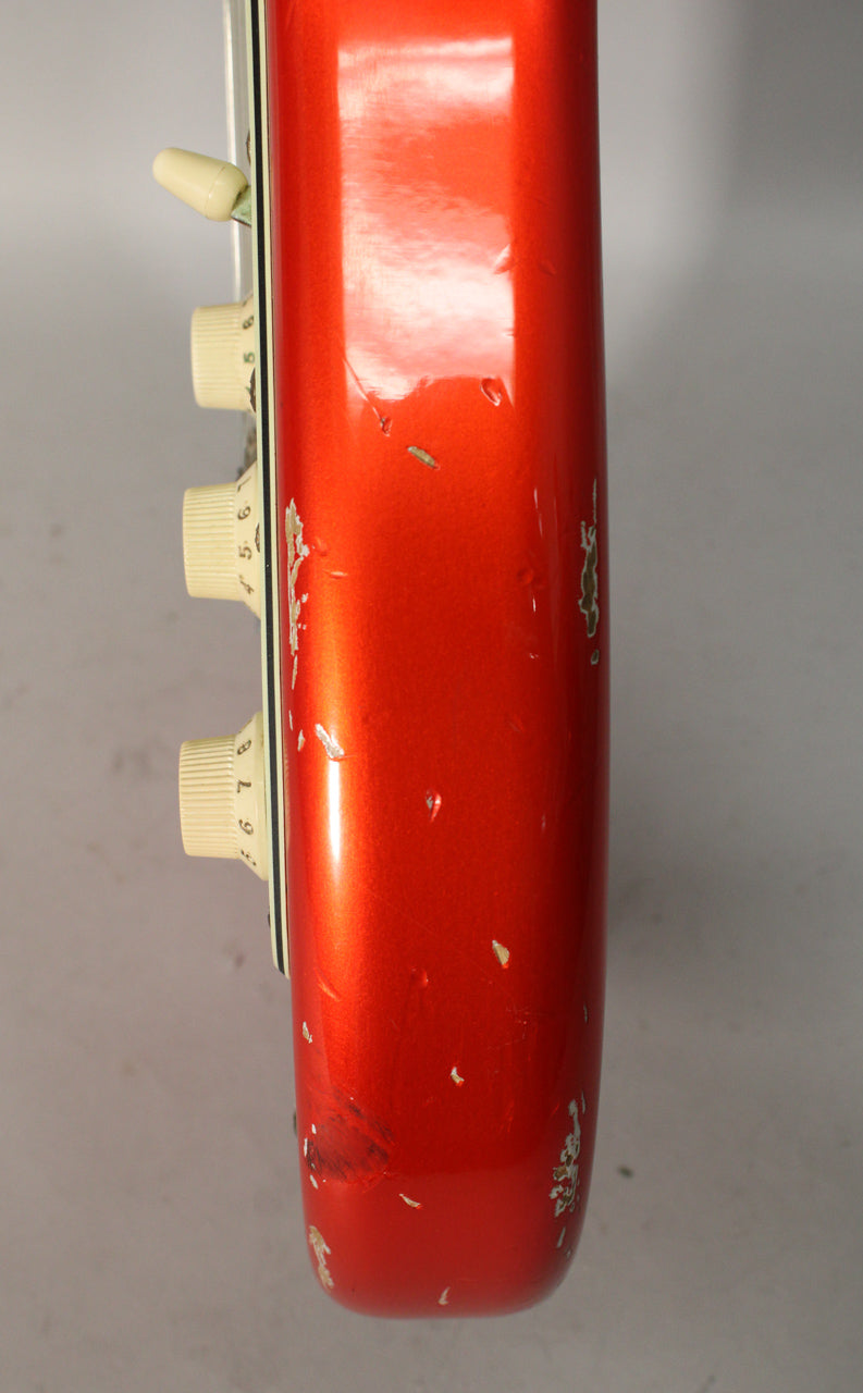 Close-up of the guitar's candy tangerine body edge, showing heavy paint chipping, scratches, and three cream control knobs with number markings.