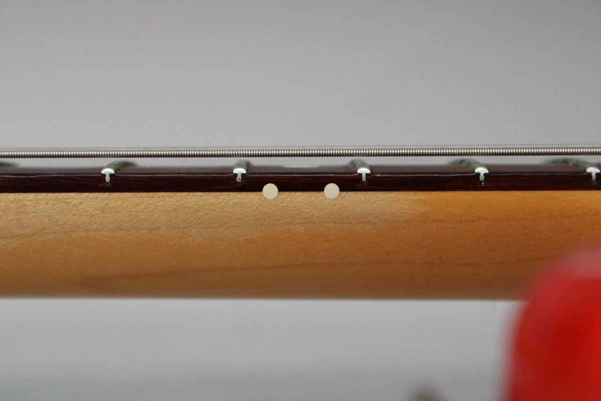 Close-up of the guitar neck's side, showing two light-colored circular fret markers on the dark fretboard and light wood neck.