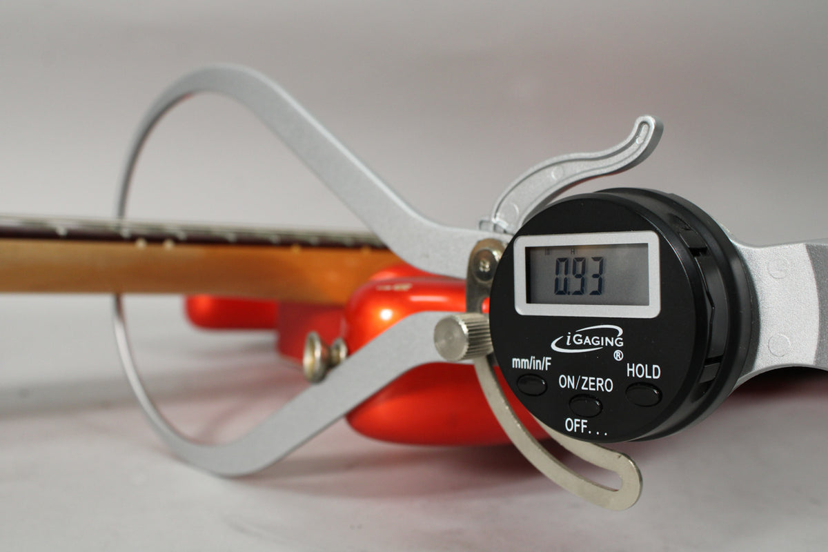 A digital caliper measures the guitar's neck relief at 0.93mm, with the tangerine body and maple neck visible in the background.