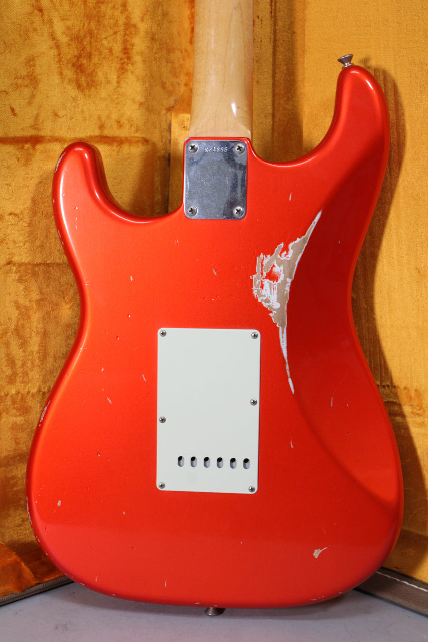The back of a tangerine Stratocaster shows a large white chip on the upper right, a white tremolo cover, and a maple neck.