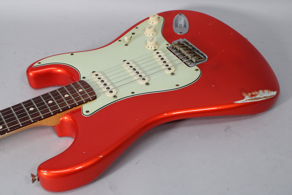 Candy Tangerine Stratocaster body, angled from the lower bout, showing a mint green pickguard, three single-coil pickups, and heavy wear on the lower edge.