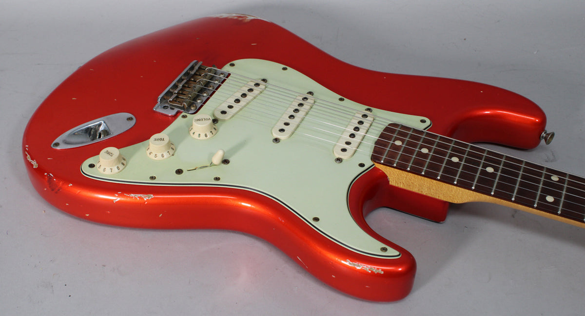 The metallic orange Stratocaster is angled right, showing its relic'd body, mint green pickguard, and three single-coil pickups.