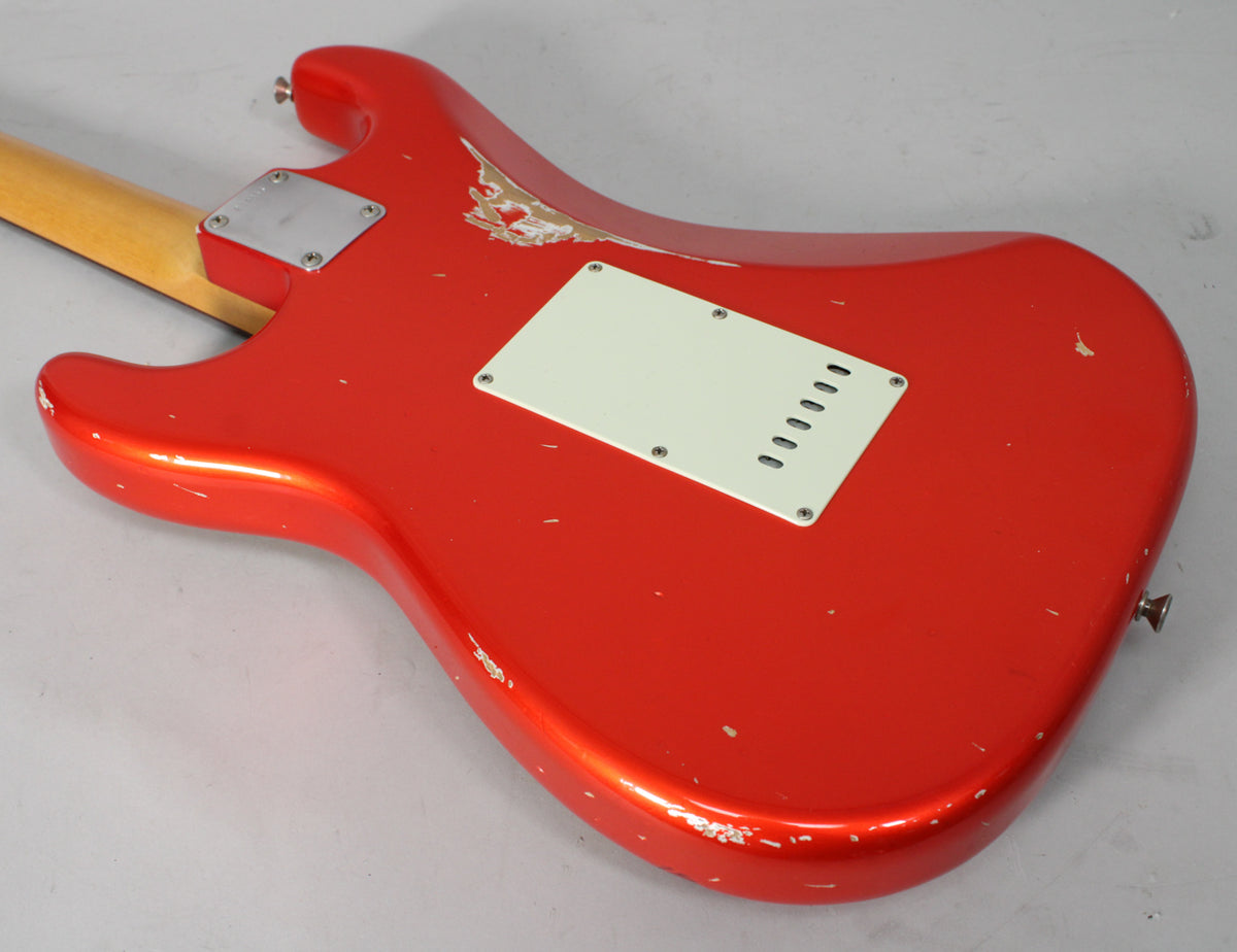 The back of a metallic red Stratocaster body with a cream tremolo cover, showing heavy relic wear and paint chips.