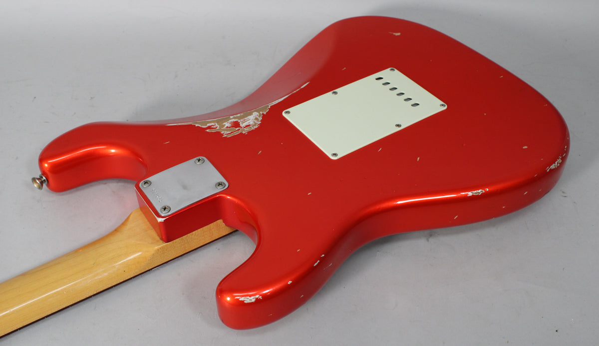 The back of a red metallic guitar body, showing a white tremolo cover, neck plate, and heavy relic wear with paint chips.