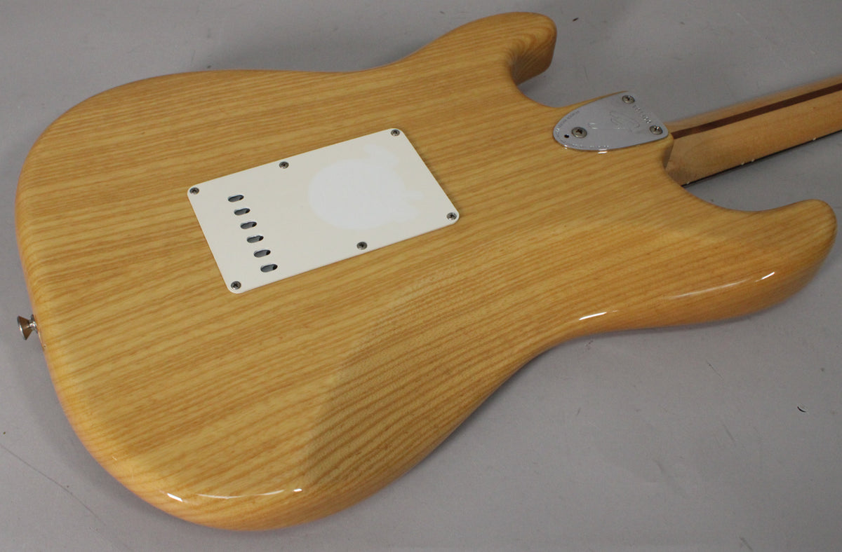 The back of a light wood grain Stratocaster body with a white tremolo cover and chrome neck plate, viewed from the lower bout.