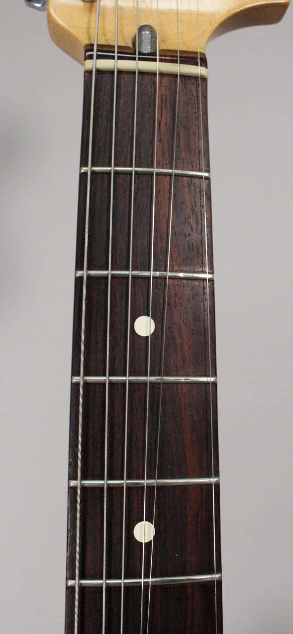 Close-up of the dark rosewood fingerboard with white dot inlays, showing light wear on the frets and a cream-colored nut.